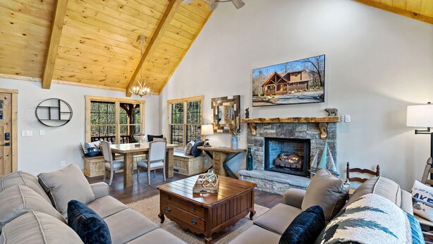 A spacious living room with a high wooden ceiling, a fireplace, and a dining area with a wooden table and chairs.