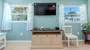 A room with teal walls, a flat-screen TV mounted above a wooden desk, a white chair, and a window with patterned curtains.
