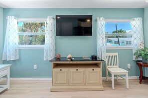 A room with teal walls, a flat-screen TV mounted above a wooden desk, a white chair, and a window with patterned curtains.