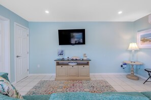 Ein Zimmer mit an der Wand montiertem Fernseher, einem Schreibtisch mit Dekoration, einer Lampe und einem gemusterten Teppich.