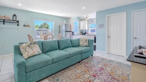 Una sala de estar con un sofá color turquesa, un tapete estampado y una cocina al fondo.
