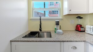 A kitchen with a granite countertop, a sink, a red blender, a white toaster, and a window with a view of buildings.