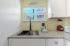 A kitchen with a granite countertop, a sink, a red blender, a white toaster, and a window with a view of buildings.