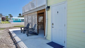 A building with a white door marked with the number 6, a covered porch with two Adirondack chairs, and a blue building in the background.