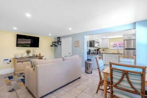 A modern living room with a sofa, a TV, and a dining area with a table and chairs.