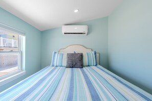 Un dormitorio con cama, almohadas, ventana y un equipo de aire acondicionado.