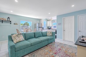 Una sala de estar con un sofá color turquesa, un tapete estampado y una cocina al fondo.