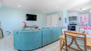 Una sala de estar con sofá, televisión, espacio de cocina con microondas y mesa de comedor con sillas.