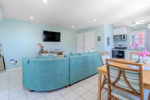 Una sala de estar con sofá, televisión, espacio de cocina con microondas y mesa de comedor con sillas.