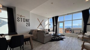 En moderne stue med stort vindue, sofa, spisebord og en reol til ski.