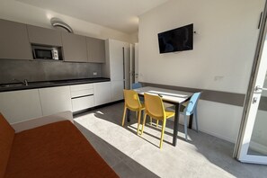 Una cucina moderna con forno a microonde, frigorifero e zona pranzo con sedie.