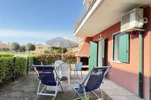Zona salotto all'aperto con sedie e tavolo, un ombrellone bianco e un edificio con un balcone.