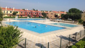 A swimming pool with multiple lanes, surrounded by a fence, and adjacent to a row of residential buildings. - Cozy Apartment With Private Garden in Bibione (San Michele al Tagliamento)