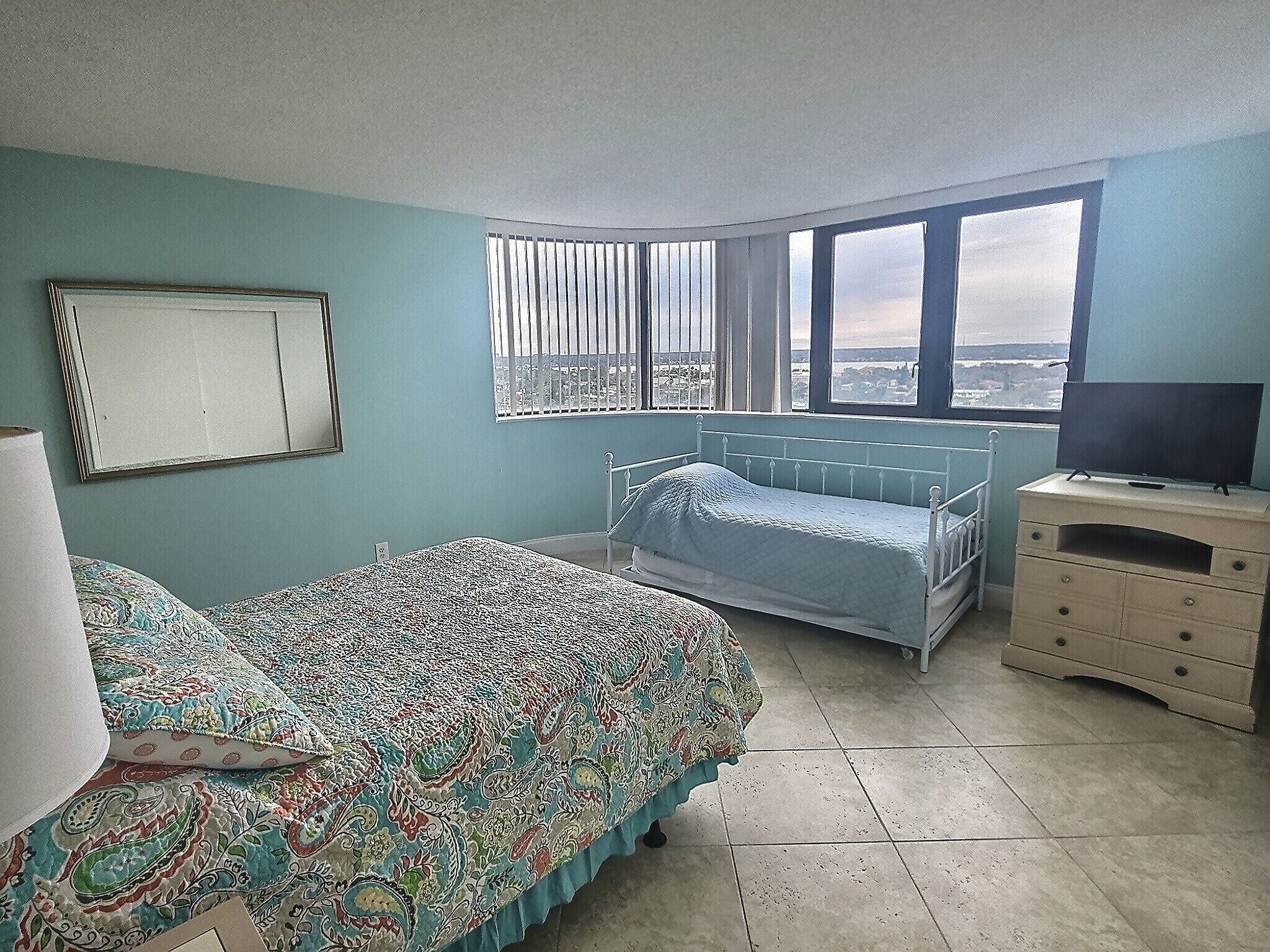 A bedroom with a bed, a dresser, a TV, and a window with a view.