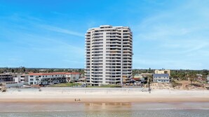 A tall, multi-story hotel with balconies, located near a beach.