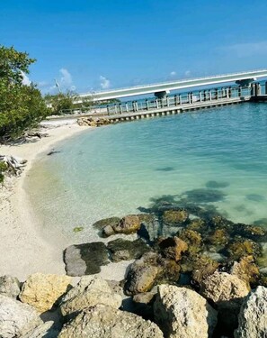 Una playa con agua cristalina, un muelle y afloramientos rocosos.