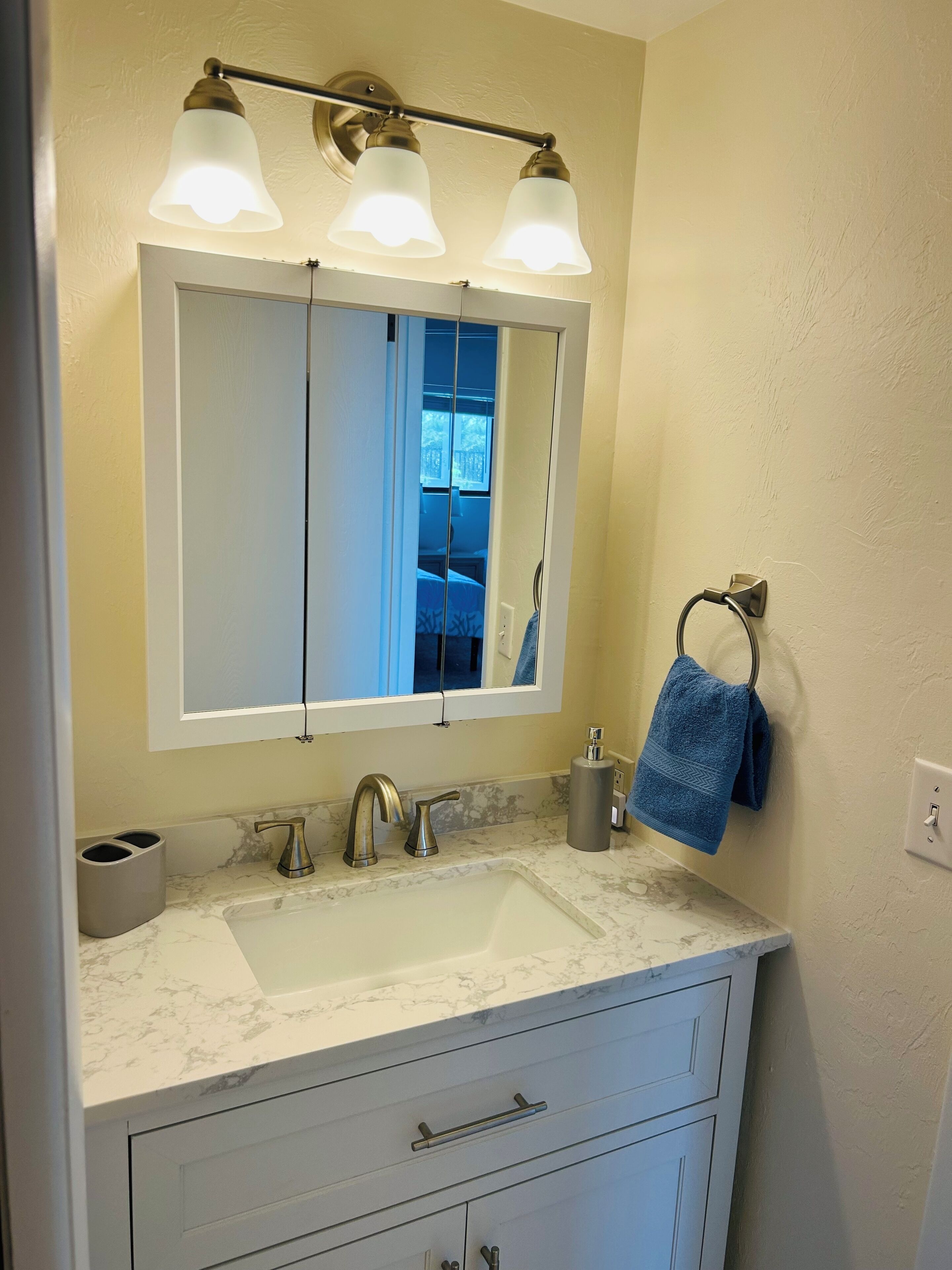 Un bagno con un lavabo in marmo bianco, uno specchio grande e un portasciugamani con un asciugamano blu.