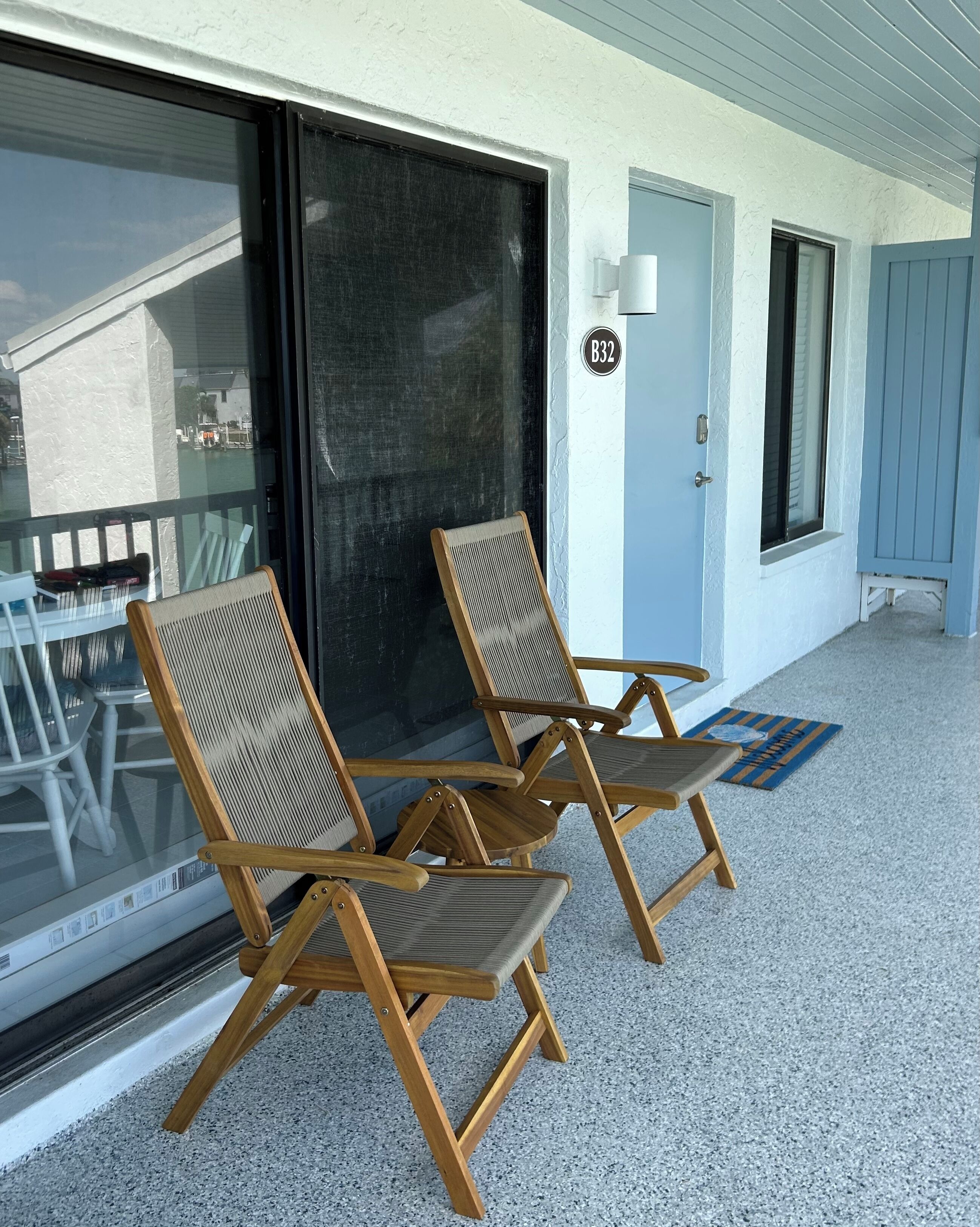 Un espace extérieur abrité, doté de chaises en bois et d’une porte vitrée donnant sur un balcon.