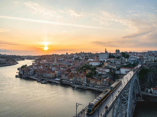 Un paisaje urbano al atardecer con un río, edificios históricos y un puente con un tren.