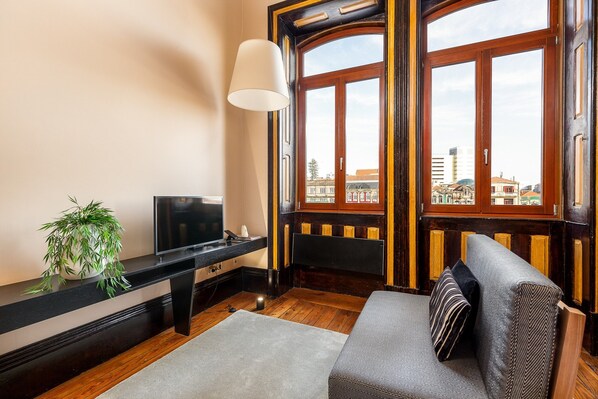 Ein Zimmer mit Fernseher, Pflanze, Sofa und Fenster mit Blick auf Gebäude.
