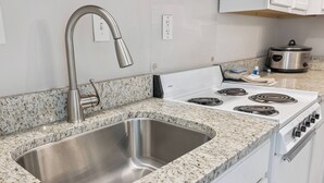 Une cuisine dotée d’un évier en acier inoxydable, d’un plan de travail en granit, de meubles blancs et d’une cuisinière.