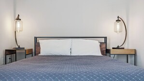 Un lit bien fait, recouvert d’une couette bleue, deux tables de chevet avec des lampes et un mur sobre.