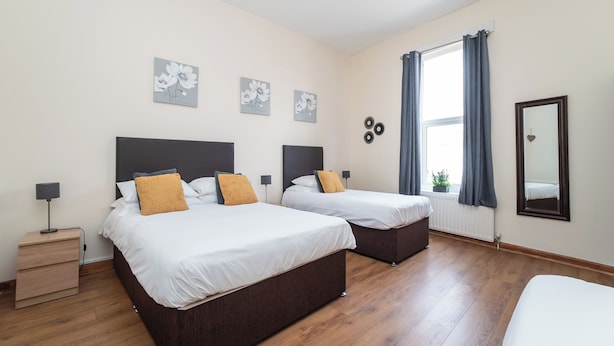 Une chambre d’hôtel avec deux lits, une table de chevet avec une lampe, une fenêtre avec des rideaux et des œuvres d’art murales.