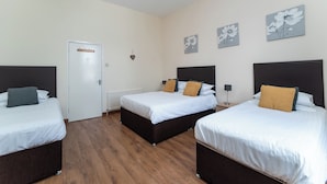 Une chambre d’hôtel avec trois lits, une porte blanche et des motifs floraux décorant le mur.