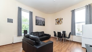 Un salon moderne avec un canapé en cuir noir, une table à manger avec des chaises et un tableau représentant un paysage urbain accroché au mur.