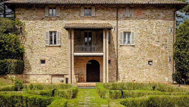 A stone building with a central entrance, a balcony, and a stone pathway leading to the entrance. - Tenuta Borgo San Michele (Gubbio)