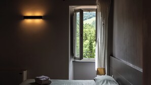 A bedroom with a bed, a window with curtains, a bedside lamp, and a wall-mounted light fixture. - Tenuta Borgo San Michele (Gubbio)