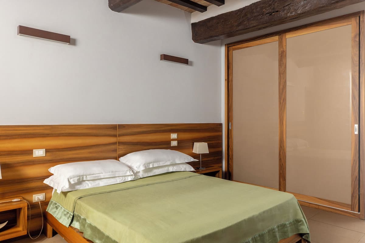 Ein Schlafzimmer mit hölzernem Kopfteil, grüner Bettdecke, weißen Kissen, einer Nachttischlampe und einem Schiebetürenschrank.