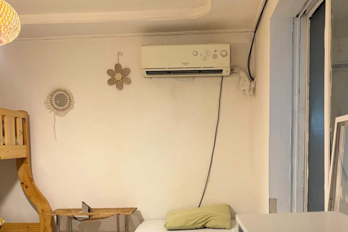 A small, compact room with a bunk bed, a desk with a laptop, an air conditioner, and a window.