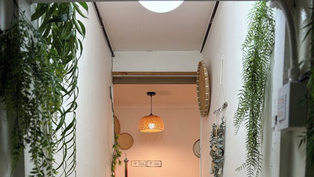 Een smalle gang met gestreepte muren, een bankje, hangende planten, een hanglamp en decoraties aan de muur.