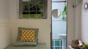 Een slaapkamer met een bed, een raam, een badkamer met een wastafel en een deur naar buiten.