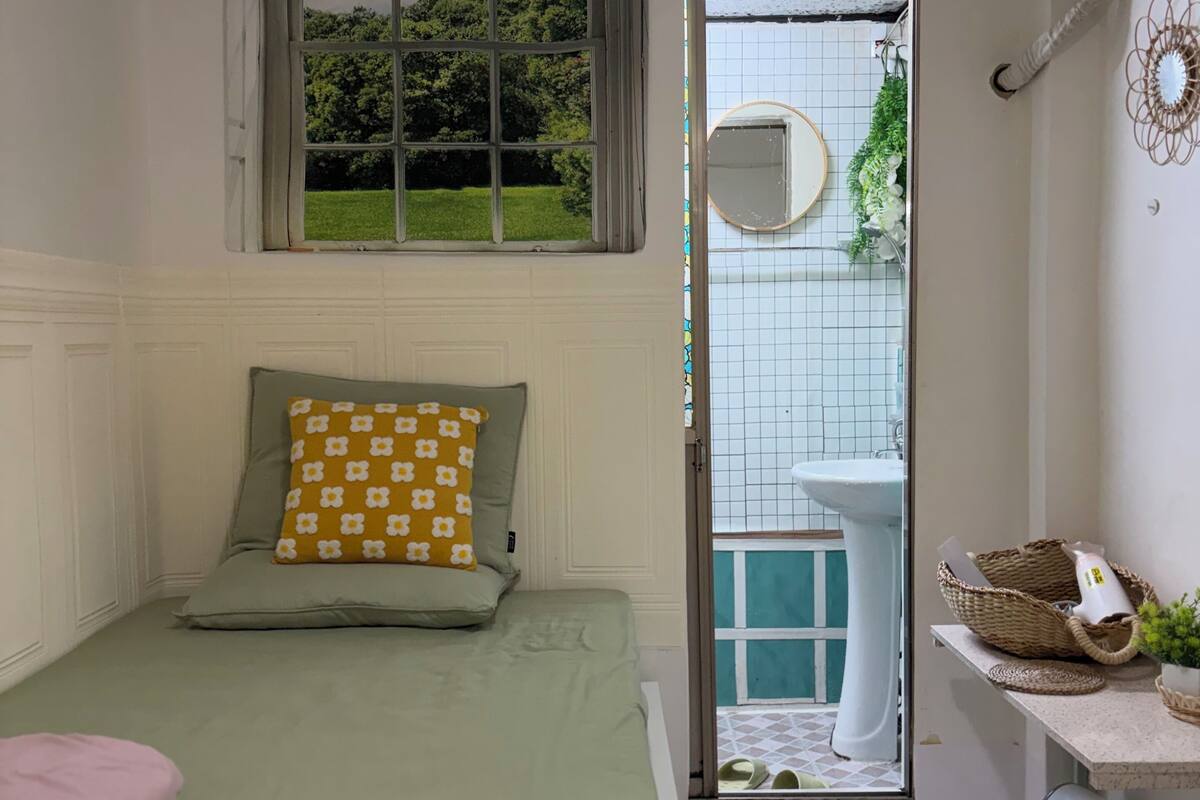 A bedroom with a bed, a window, a bathroom with a sink, and a door leading outside.