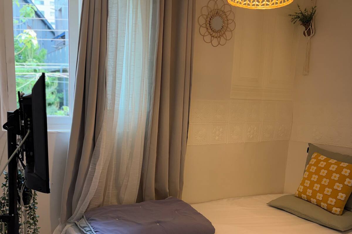 A bedroom with a bed, curtains, a hanging light fixture, and a window.