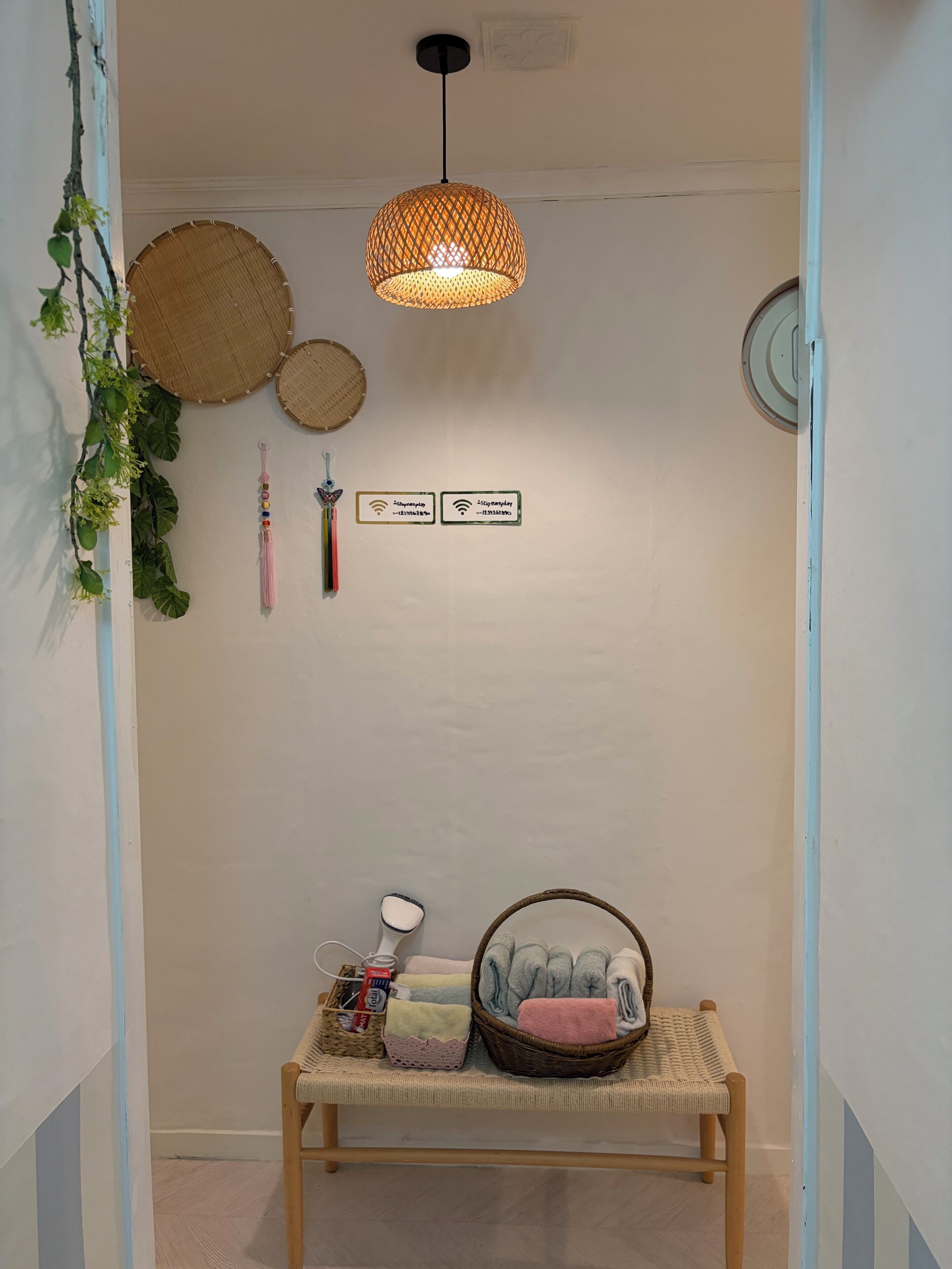 A hallway with a woven light fixture, wall-mounted woven baskets, a bench with towels, and a wall-mounted Wi-Fi sign.