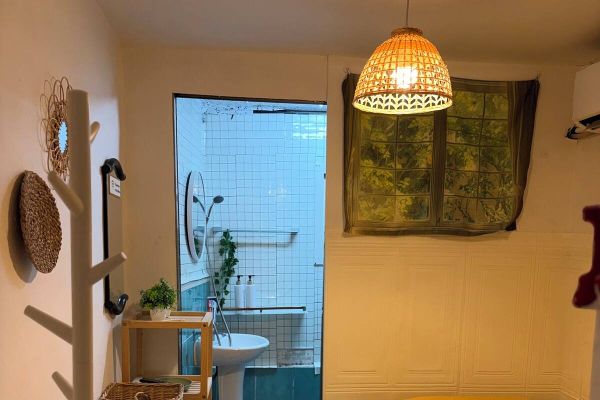 A compact room with a bed, a hanging light fixture, a small sink, and a window with a view.