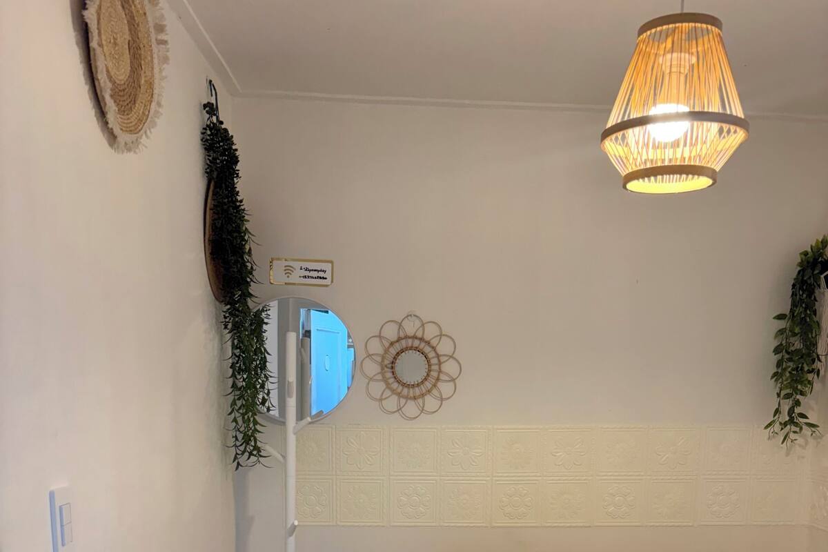 A bedroom with a bed, a bedside table, a mirror, and a hanging light fixture.