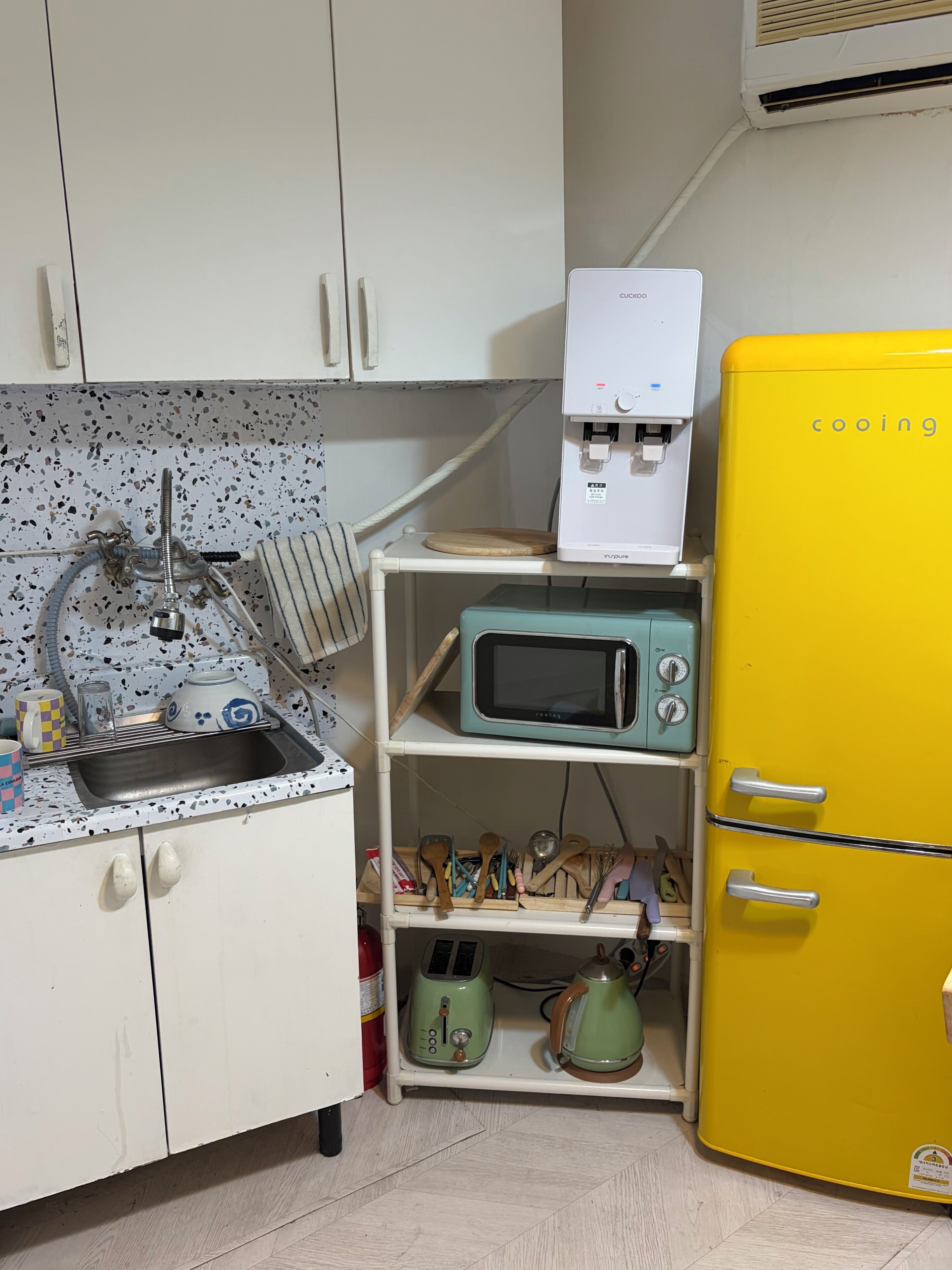 A kitchen with a sink, a water dispenser, a microwave, a toaster, and a yellow refrigerator.