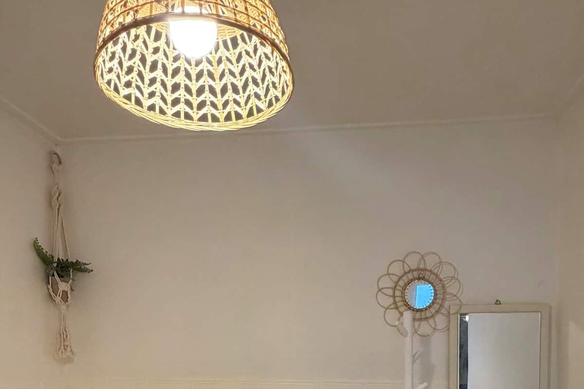 A room with a bed, a standing lamp, a mirror, and a wall-mounted macrame decoration.