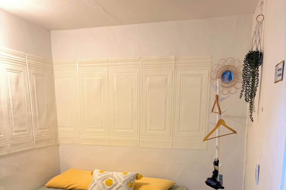 A bedroom with a bed, a floor lamp, and a wall-mounted plant.