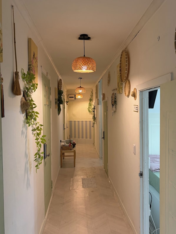 Un couloir avec un luminaire décoratif au plafond, un banc sur lequel sont posés divers objets, et une porte donnant sur une pièce.