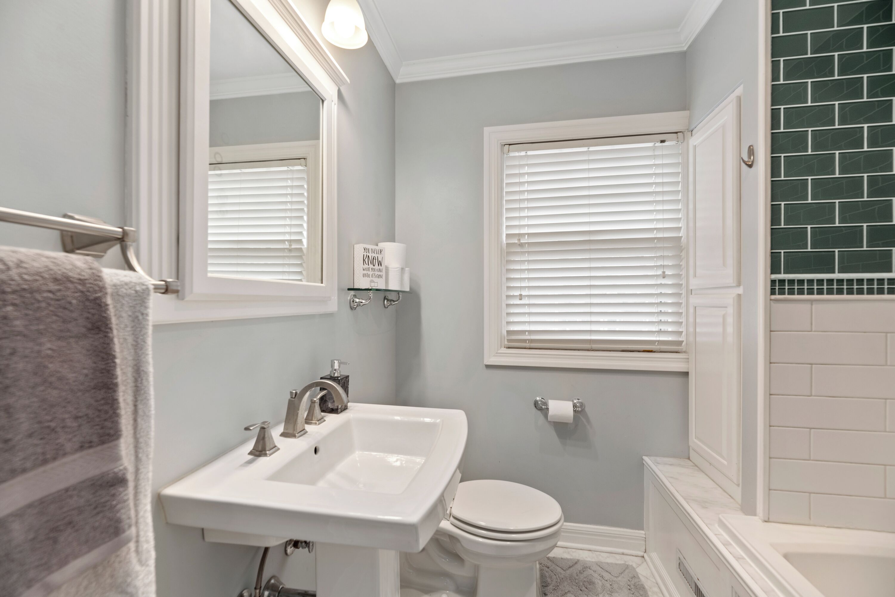 A bathroom with a white sink, toilet, and a window with blinds.