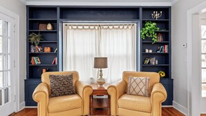 Un salon comprenant deux fauteuils en cuir, une petite table en bois, un lampadaire et une bibliothèque remplie de livres et d’objets décoratifs.