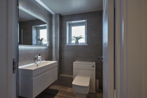 A modern bathroom with a white sink, mirror, and toilet. There are two windows providing natural light. - 2022 Modern Home In Central Hayle With Parking (Hayle)