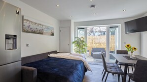 Un dormitorio moderno con una cama, un comedor con sillas, un televisor y un ventanal grande.