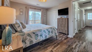 A bedroom with a bed, a nightstand, a lamp, a ceiling light, a wardrobe, a television, and a view of the outside. - Beachside Serenity Awaits at 'Knot A Worry'" (Surf City)