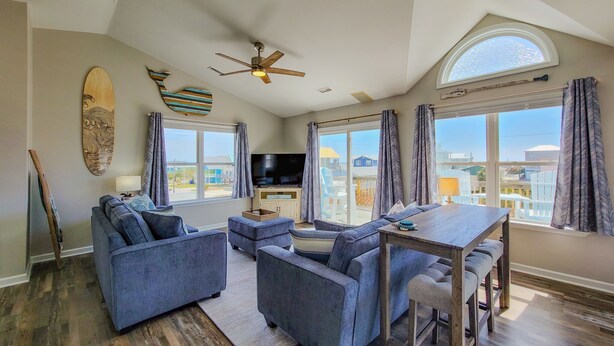 A spacious living room with a large window, a ceiling fan, and a flat-screen TV. - Beachside Serenity Awaits at 'Knot A Worry'" (Surf City)